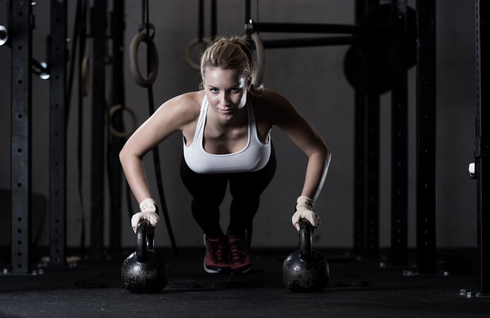 Young strong girl doing push-ups na kettlebells